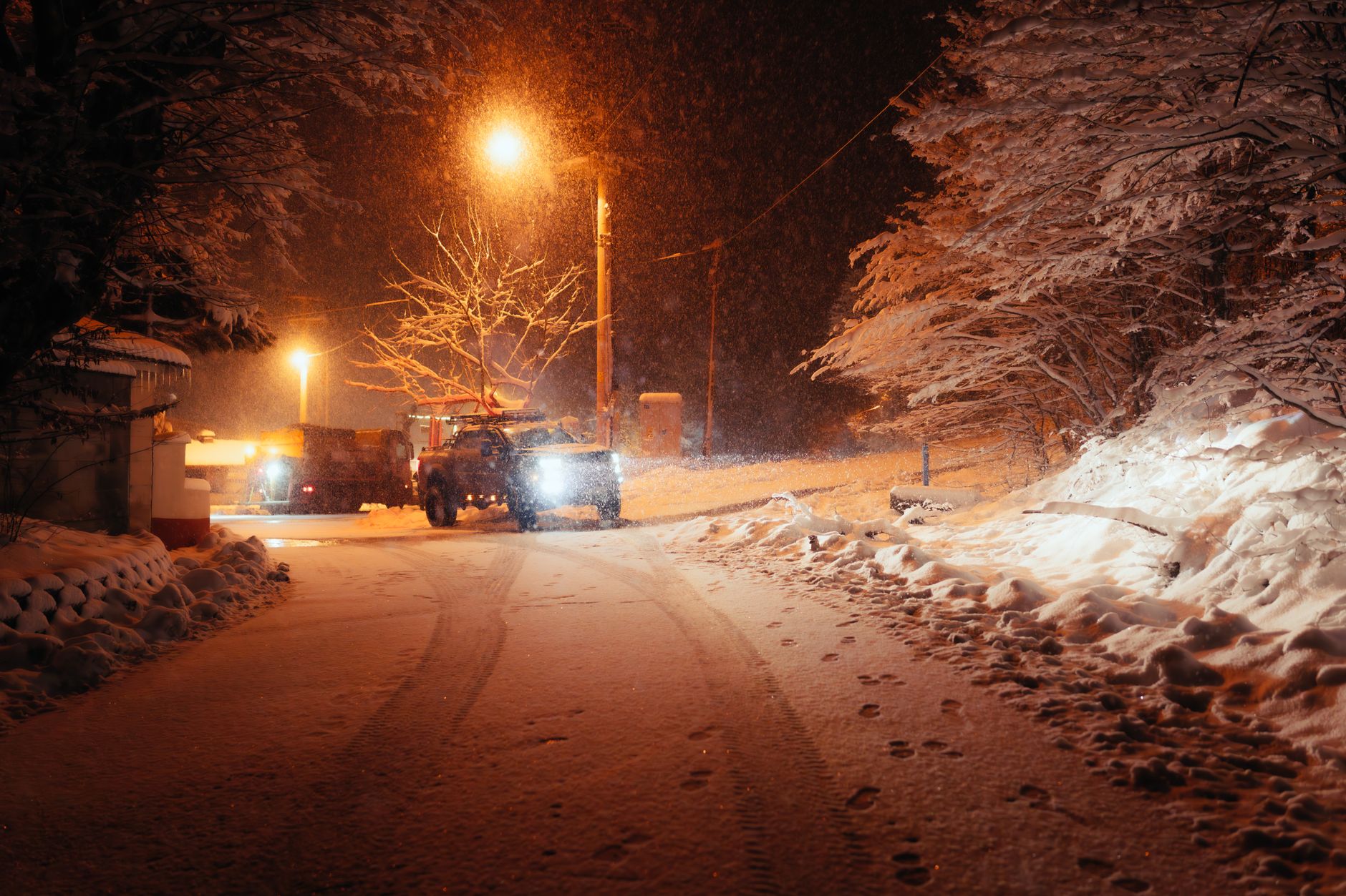 Pickup truck parked in a snowy driveway with an extension cord running toward a house