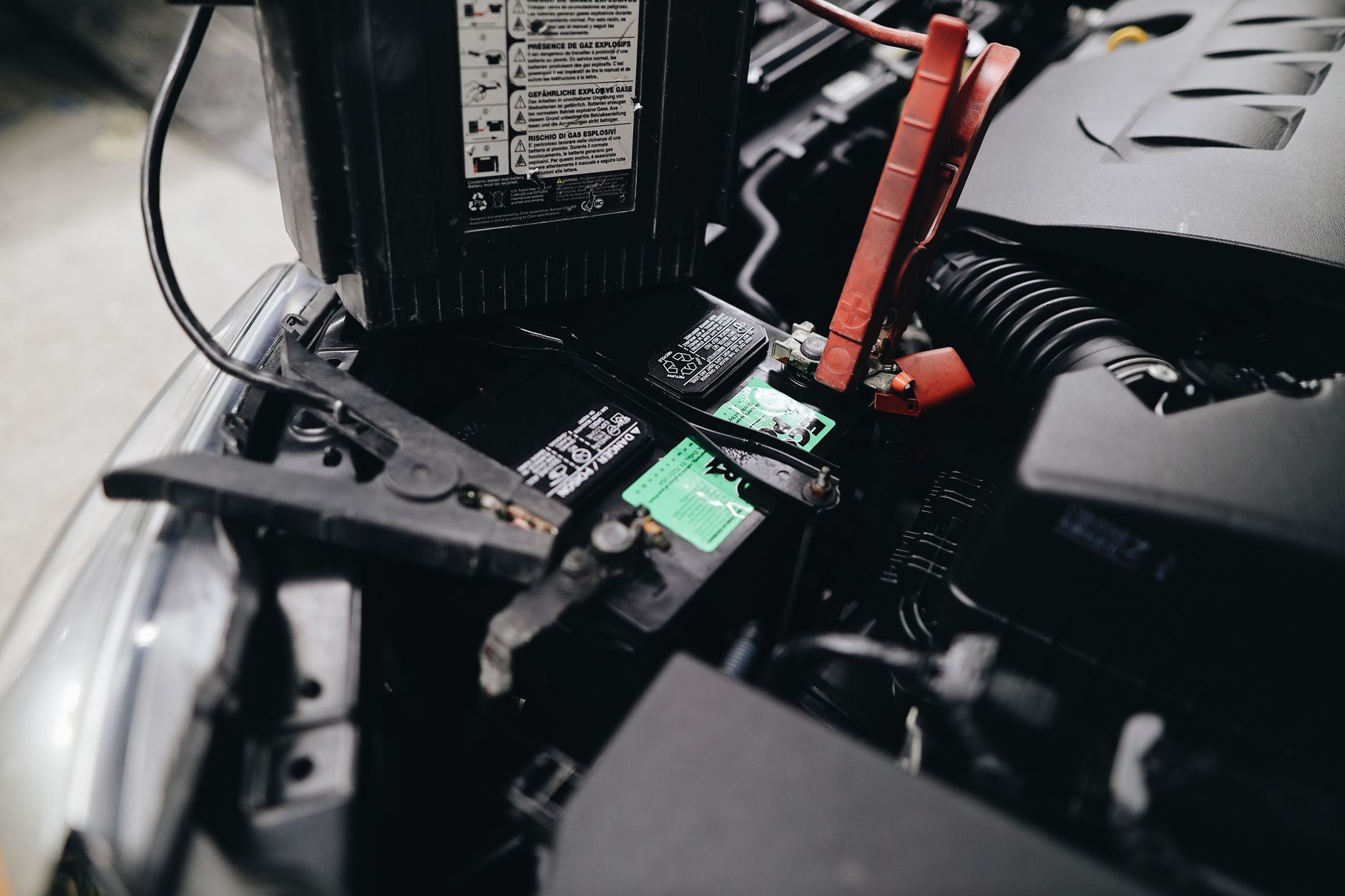 Hands connecting red and black jumper cable clamps to a car battery terminal