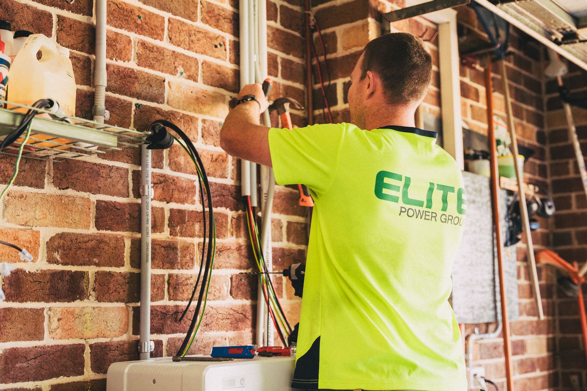 A licensed electrician wiring a residential battery backup unit next to a home electrical panel